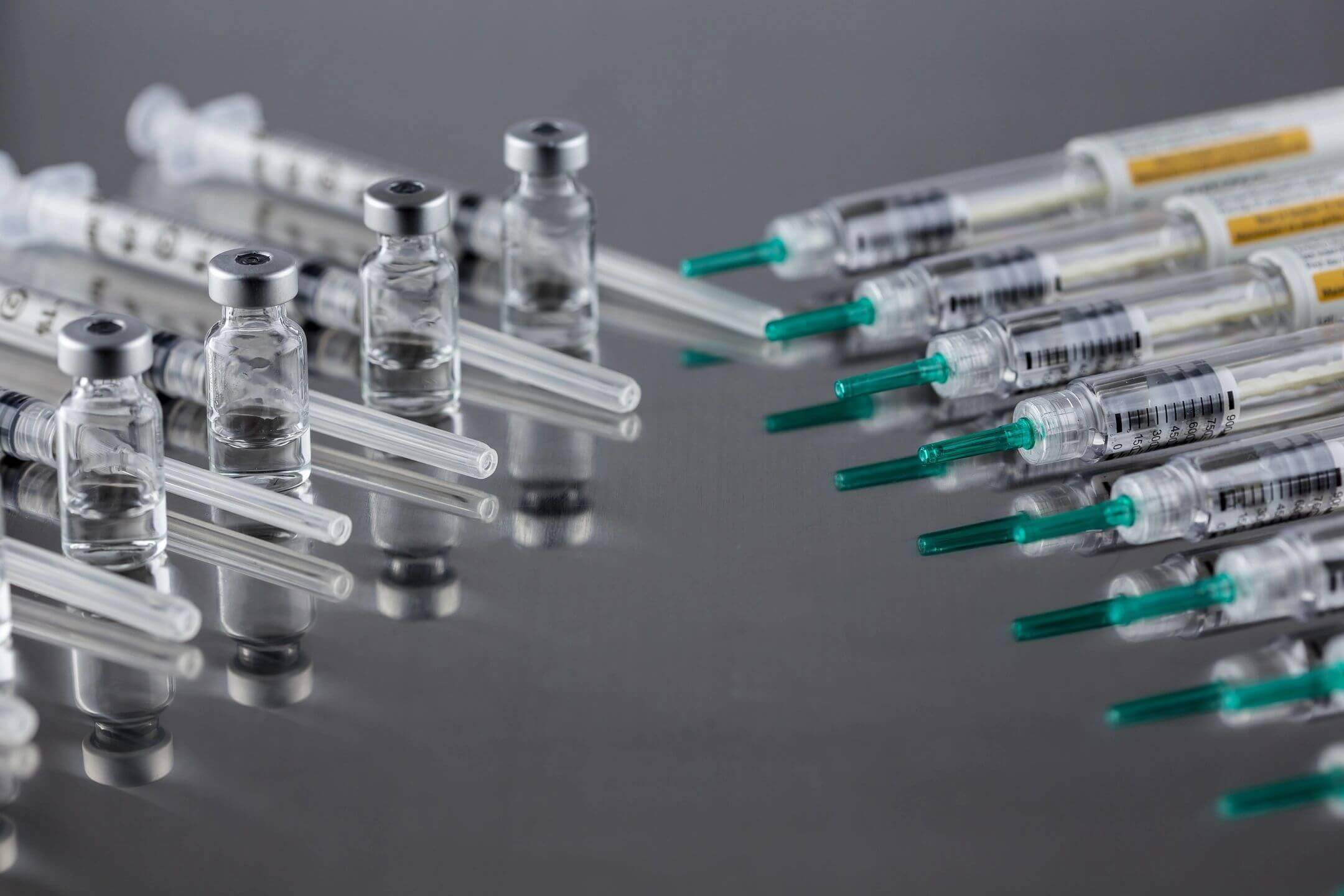 Several syringes filled with clear liquid on a reflective surface.