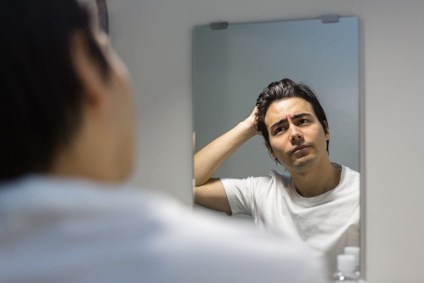 Man looking thoughtfully at his reflection in the mirror.