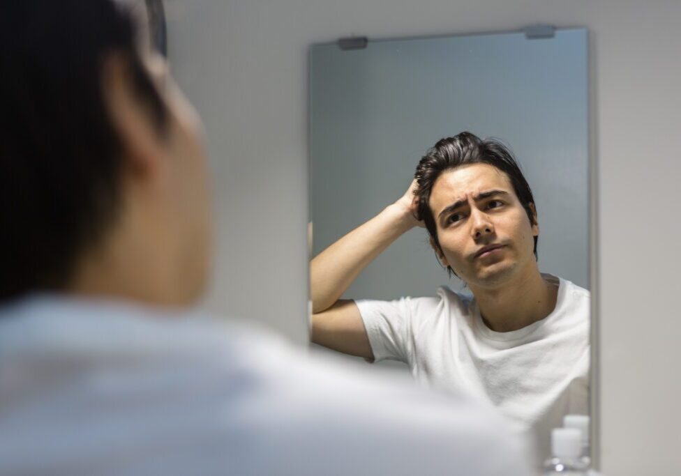 Man looking thoughtfully at his reflection in the mirror.