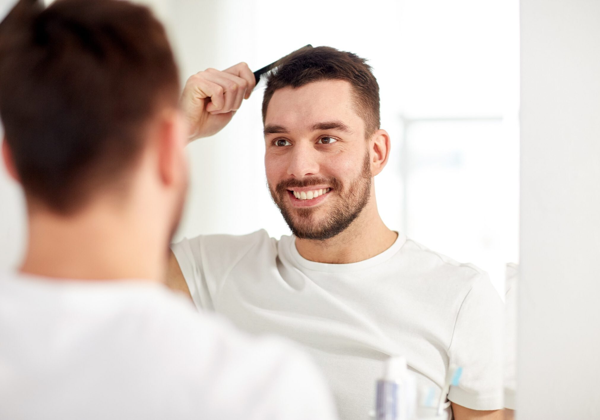 A man combing his hair in front of a mirror, smiling.