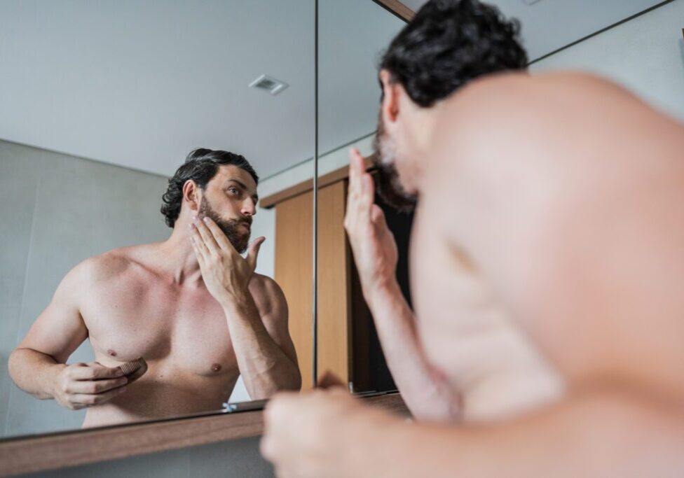 Man examining his facial skin in front of a bathroom mirror.