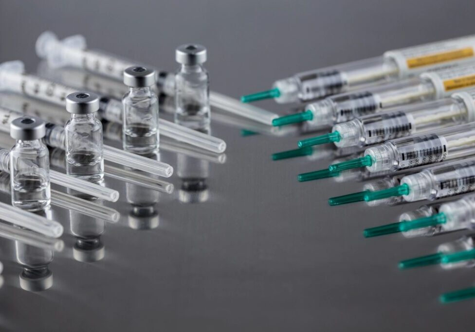 Several syringes filled with clear liquid on a reflective surface.