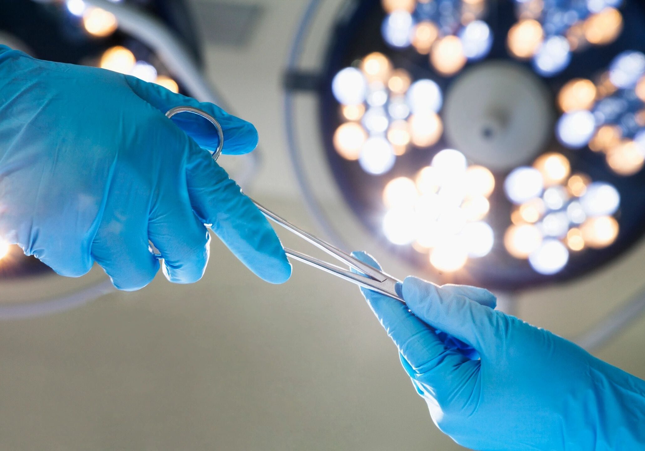 Surgeon wearing blue gloves holding a surgical suture in a sterile operating room.