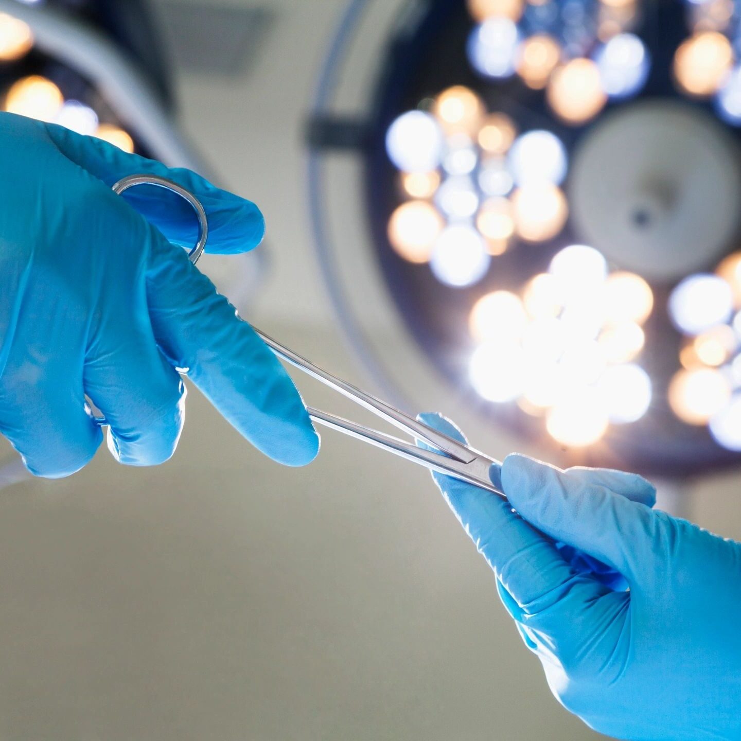 Surgeon wearing blue gloves holding a surgical suture in a sterile operating room.